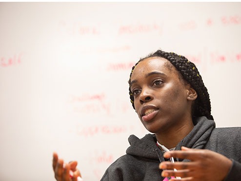 A female student gestures in front of a whiteboard.