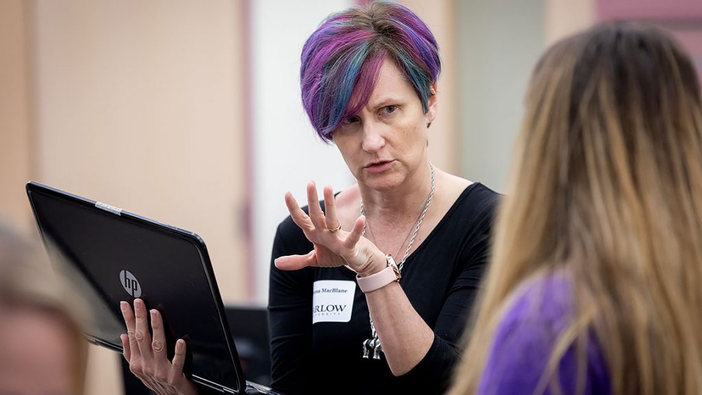 A woman holds a laptop and gestures while talking to a student at an academic support workshop.