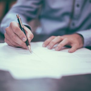 A hand is holding a pen over accreditation papers.