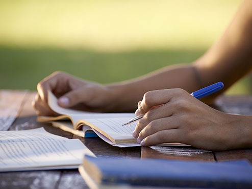 A student reads a book while holding a pen at an outdoor table