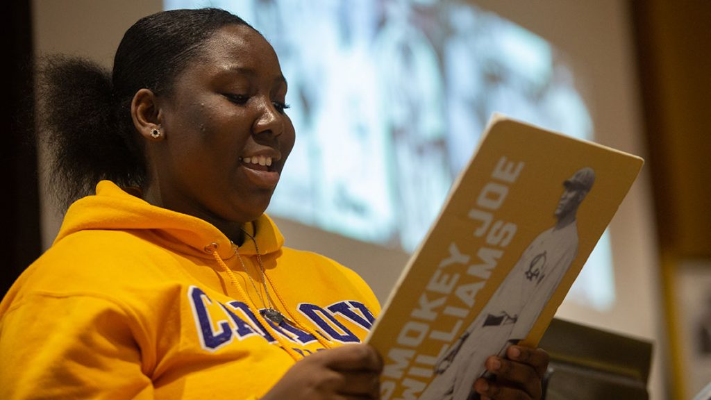 A female student wearing a Carlow sweatshirt reads from a clipboard with a baseball player on the back of it.