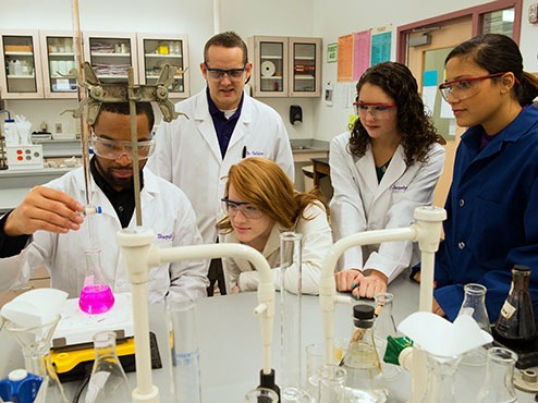 Carlow Noyce Scholarship students wearing lab coats look at pink liquid in a flask.