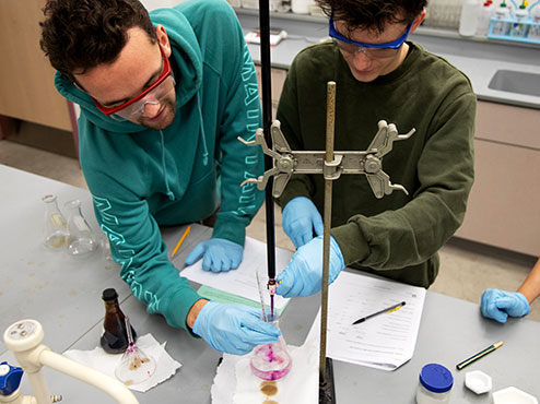 Two chemistry students work together on an experiment in class. They are filling a beaker with liquid.