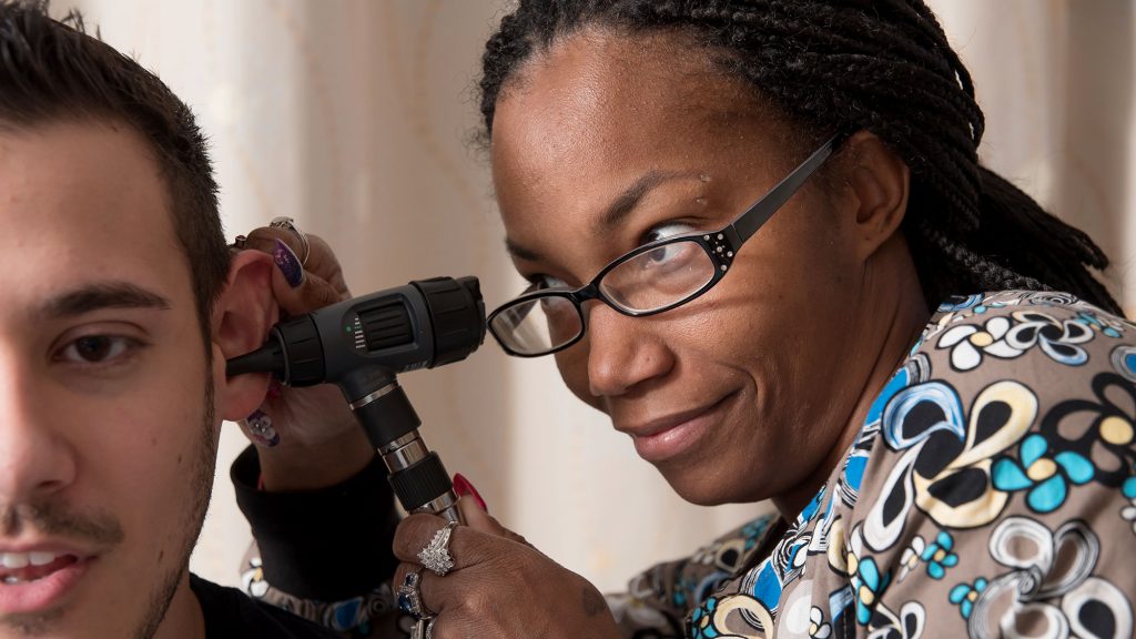 A family nurse practitioner examines the ear of a patient. She wears glasses and is looking through her otoscope.