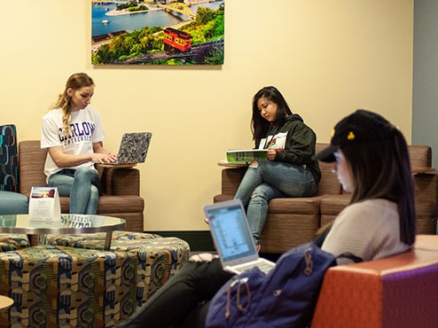 Three students are sitting in separate pieces of lounge furniture while studying.