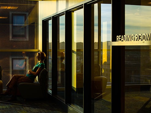 A student sits in a chair next to windows that show nearby buildings.