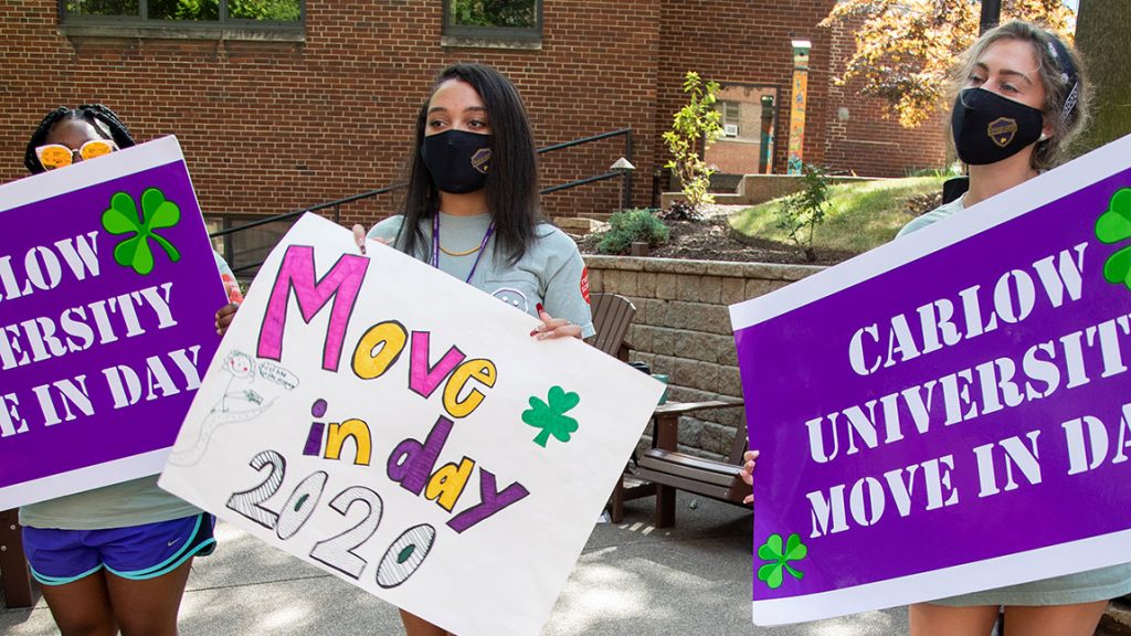 Resident assistants wearing masks hold big signs welcoming new students on Move In Day.