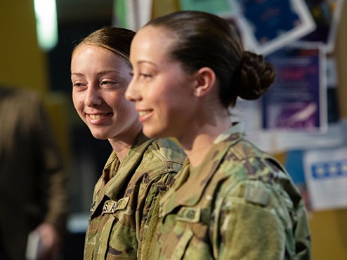 Two uniformed female ROTC students walk in a campus hallway.
