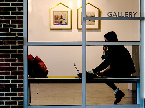 A student looks at a laptop on a bench inside a window in an art gallery.