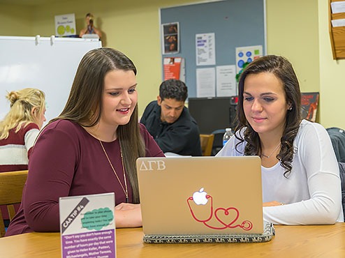 Two students in a tutoring session look at an open laptop while sitting at a table.