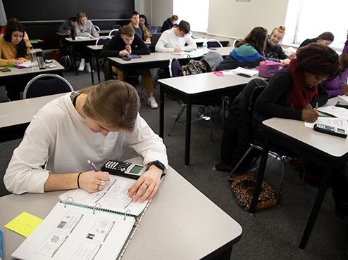 Students at work with calculators and notebooks at tables in a classroom.