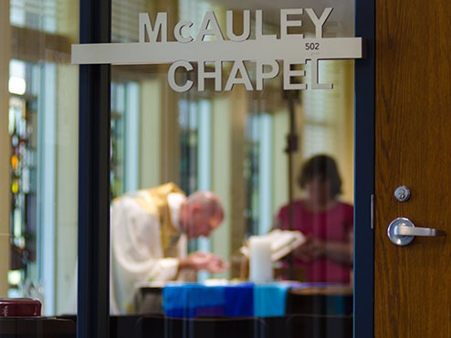 A priest with outstretched hands is bent over a table with a woman in front of him inside McCauley Chapel.