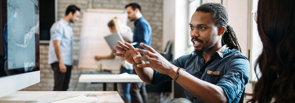 A business management student gestures at content on a computer while talking with another student.