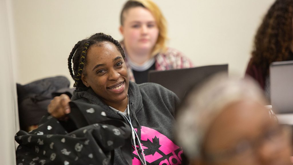 A Carlow students smiles at the camera during class. She is surrounded by other classmates.