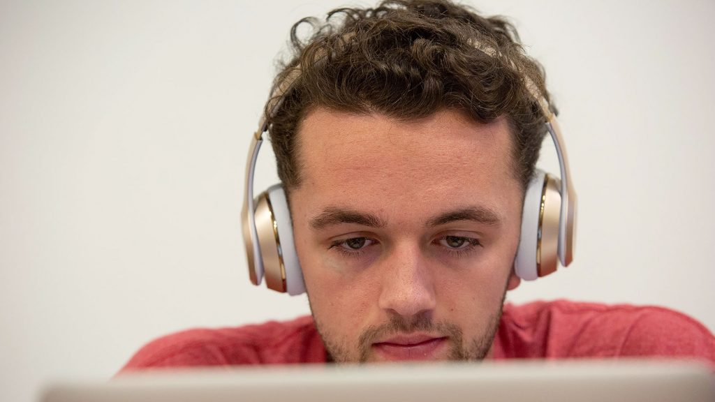 A Carlow student listens on his headphones as he works on his laptop.