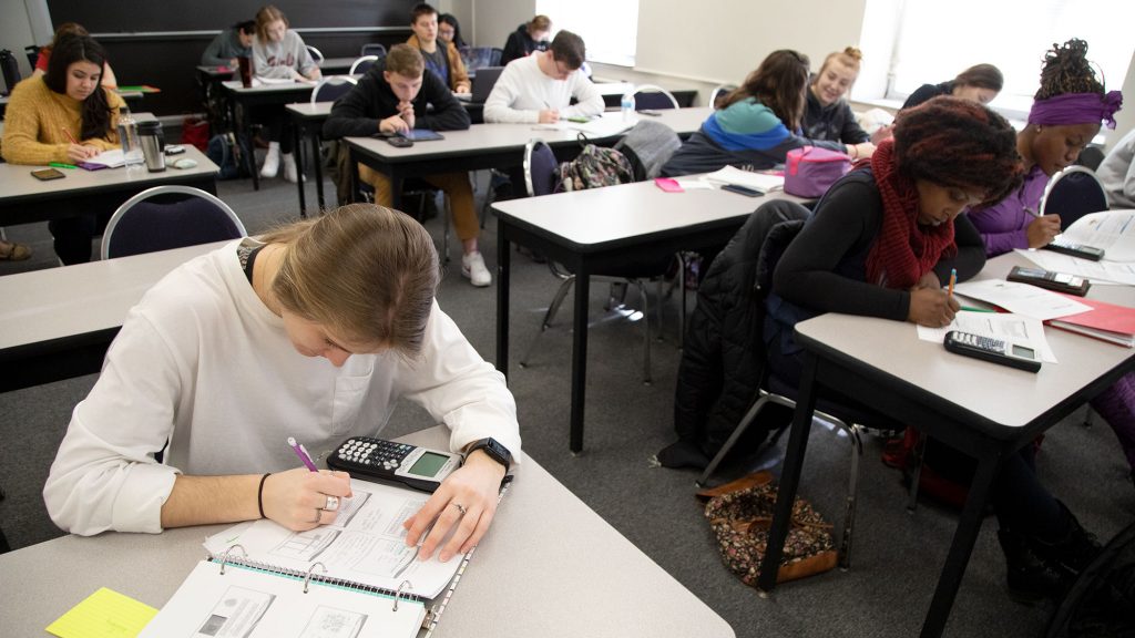 Students work on their assignment during class. All are seated at desks of 2-3 people.