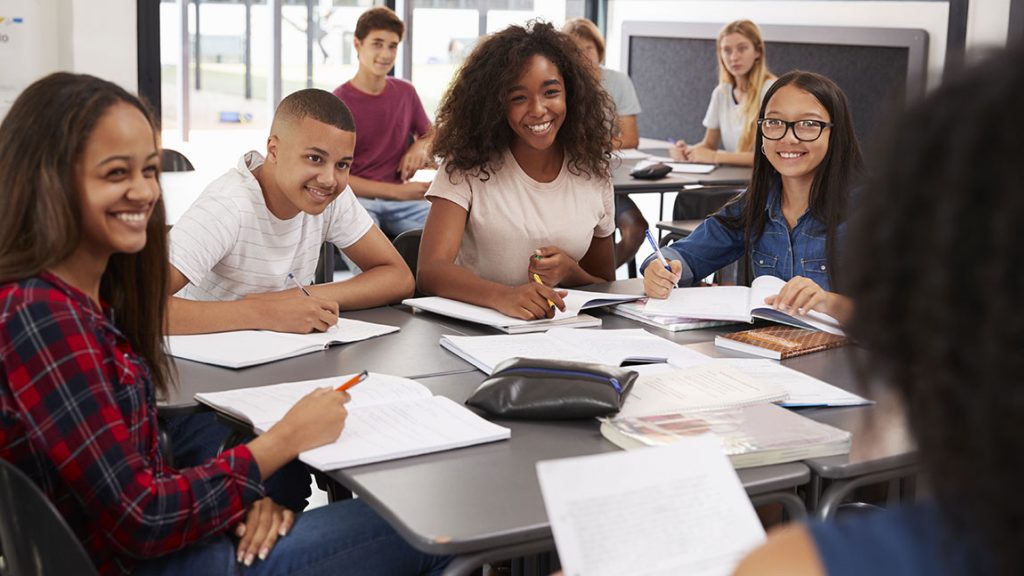 High school kids looking to teacher sitting at their desk