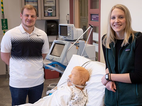 Students in class standing next to simulation patient and smiling