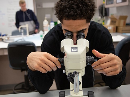 A male student looking into a microscope in class.
