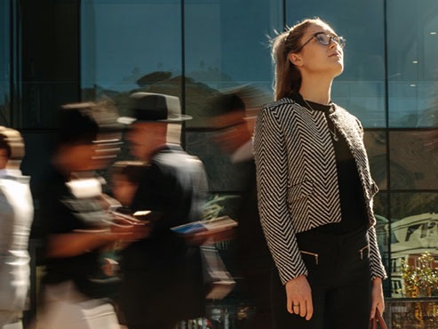 Woman dressed in business attire standing outside of a building, looking towards the sky.
