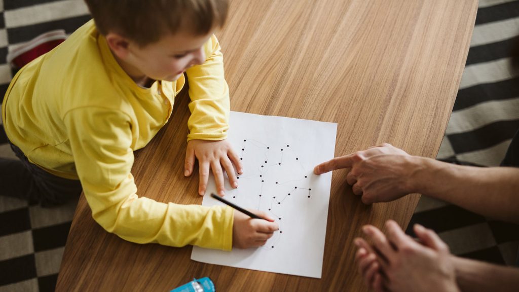 Boy kneeling on the floor and connecting dots on a piece of paper