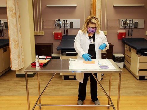 Woman in lab coat and gloves in Carlow's simulation lab at a table.