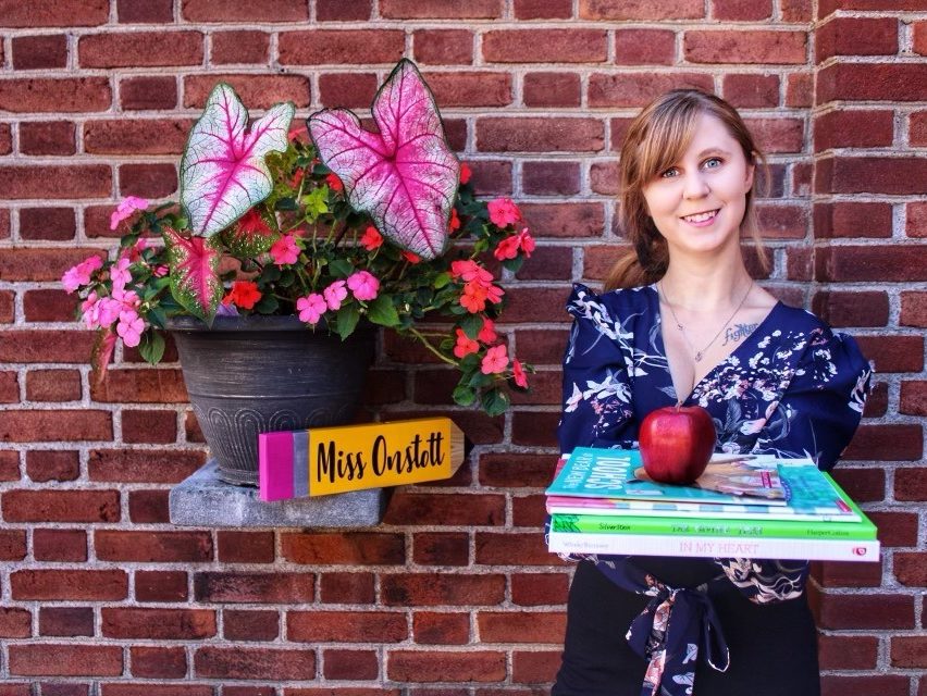 Samantha Onstott stands in front of a brick wall holding a cake.