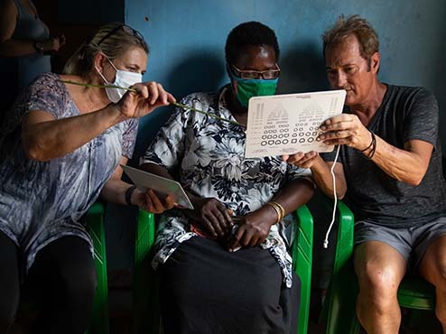 Two adults conduct an eye exam for a Ugandan woman. They are sitting pointing at a piece of white paper.