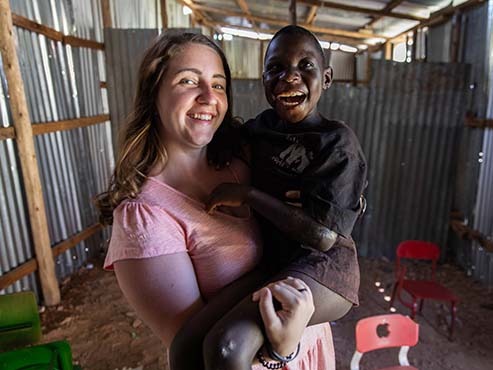 A woman holding a Ugandan child, both are smiling.