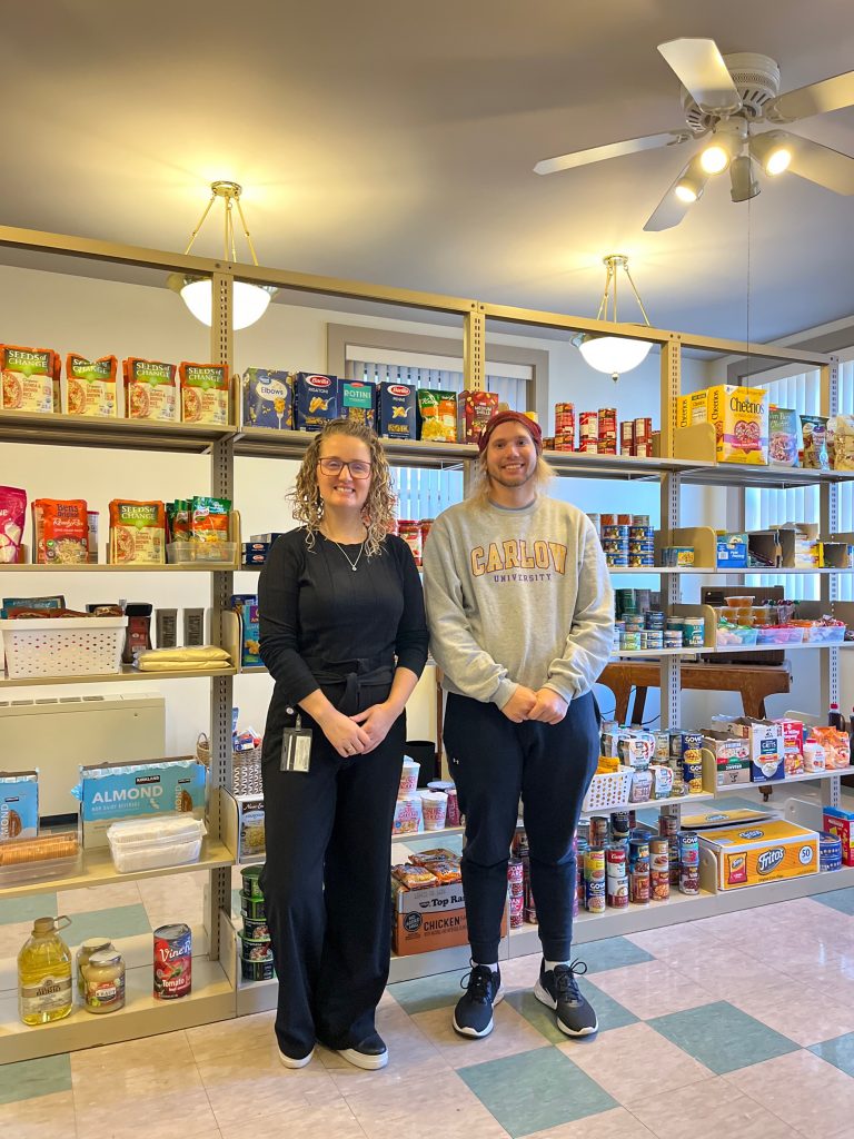 Two people standing in front of shelves full of food.