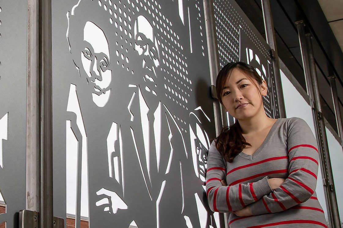 Female student smiling next to art mural on a campus