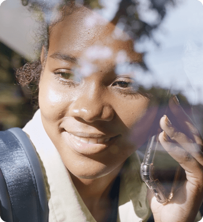 A student outdoors smiling while talking on a mobile phone