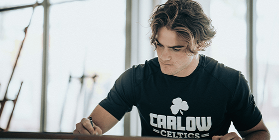 A Carlow University student in a Carlow Celtics T-shirt working at a studio table