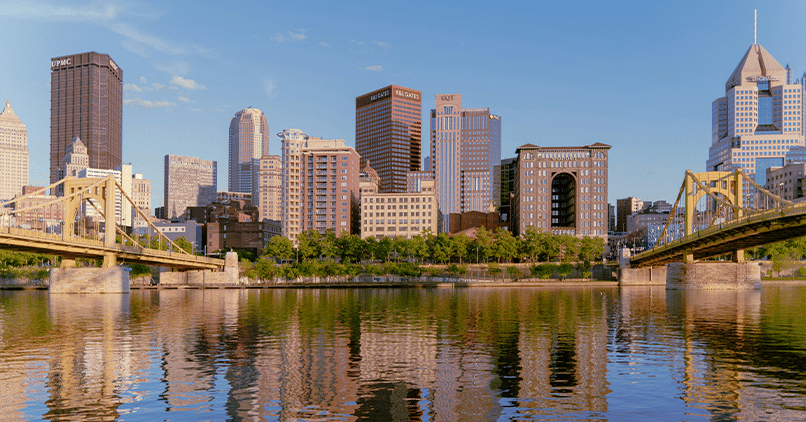 The downtown Pittsburgh skyline and a yellow bridge reflected in the river